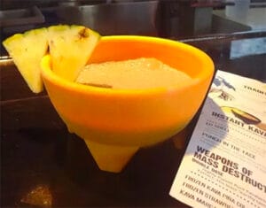 A drink of kava in a yellow cup with pineapple wedge on the side